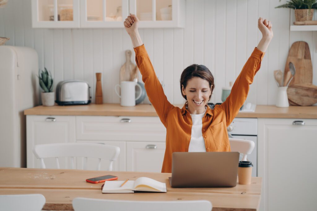 Excited successful business woman in front of laptop raising hands in joy to illustrate 5 Ways to Help Clients Value and Understand Your Work
