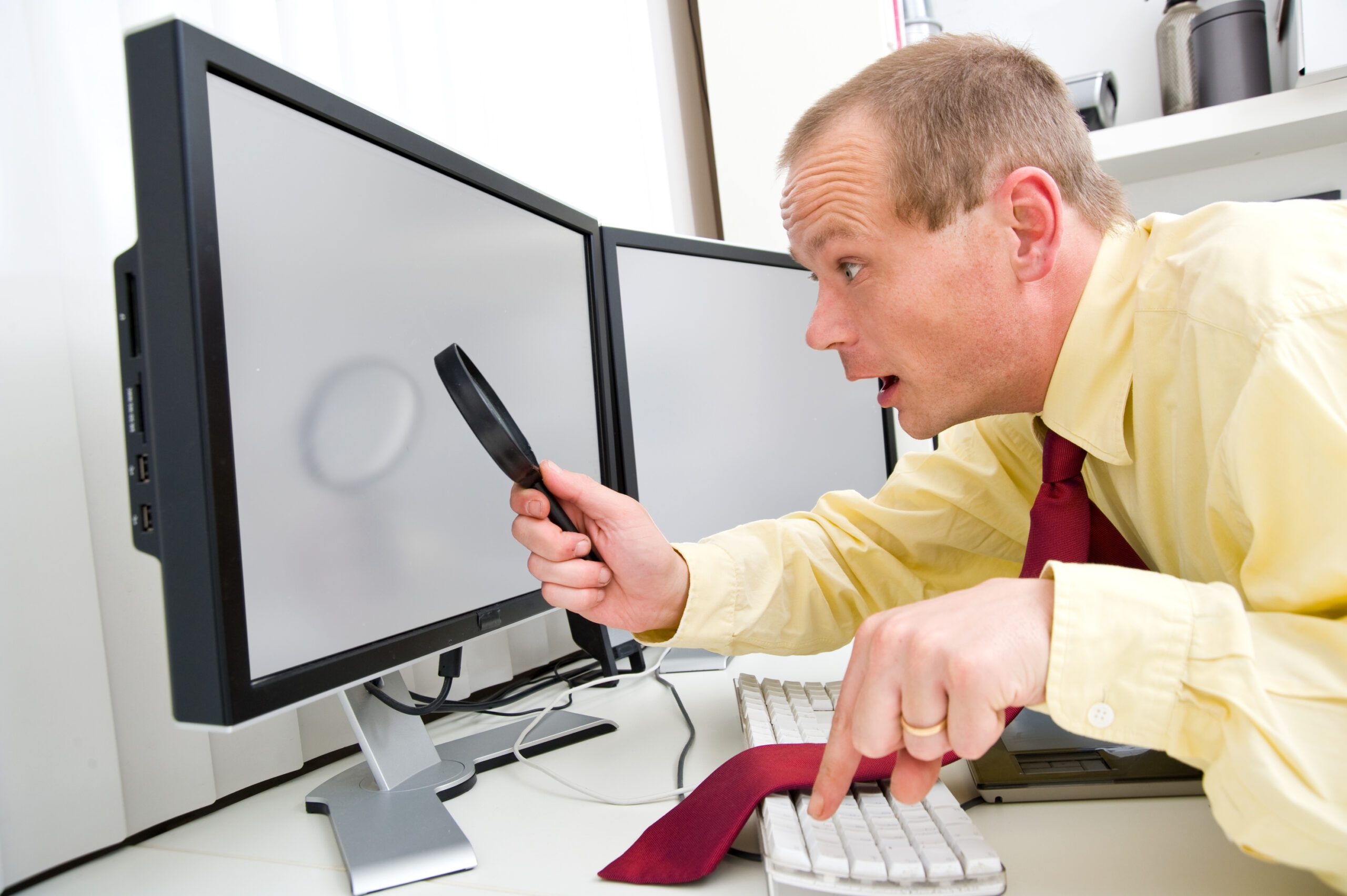 A man in a red tie leaning toward a computer monitor with a magnifying glass to illustrate AI Content Writers What They Get Right & What They Muck Up.