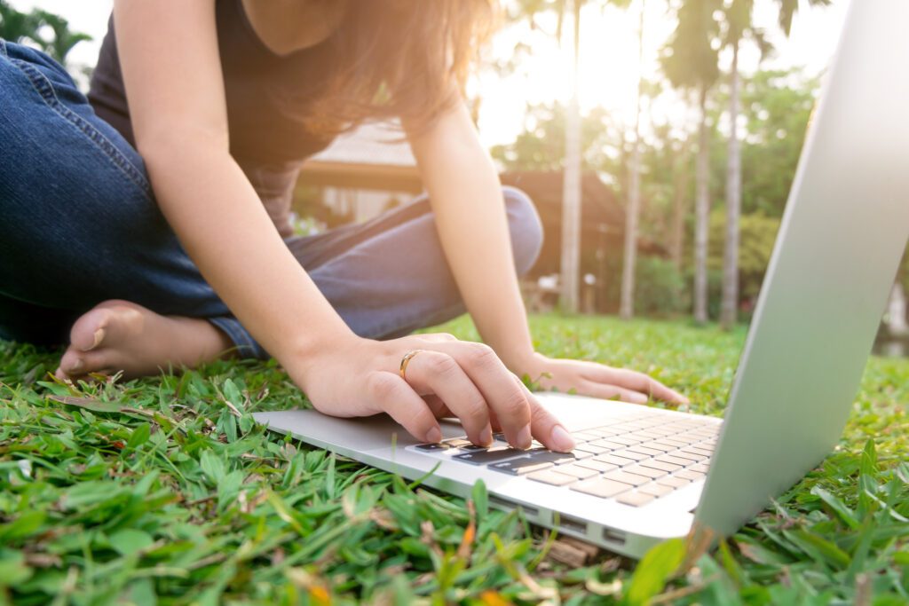 young woman using laptop at outdoors on the grass with sunshine in the background to illustrate E-A-T Improve Expertise, Authoritativeness, Trustworthiness
