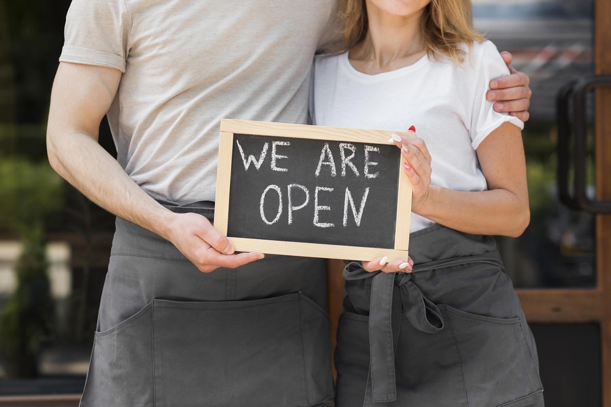 Couple with a "we are open" sign for their small business,