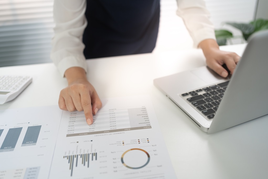 Business person analyzing data on a sheet with a laptop.